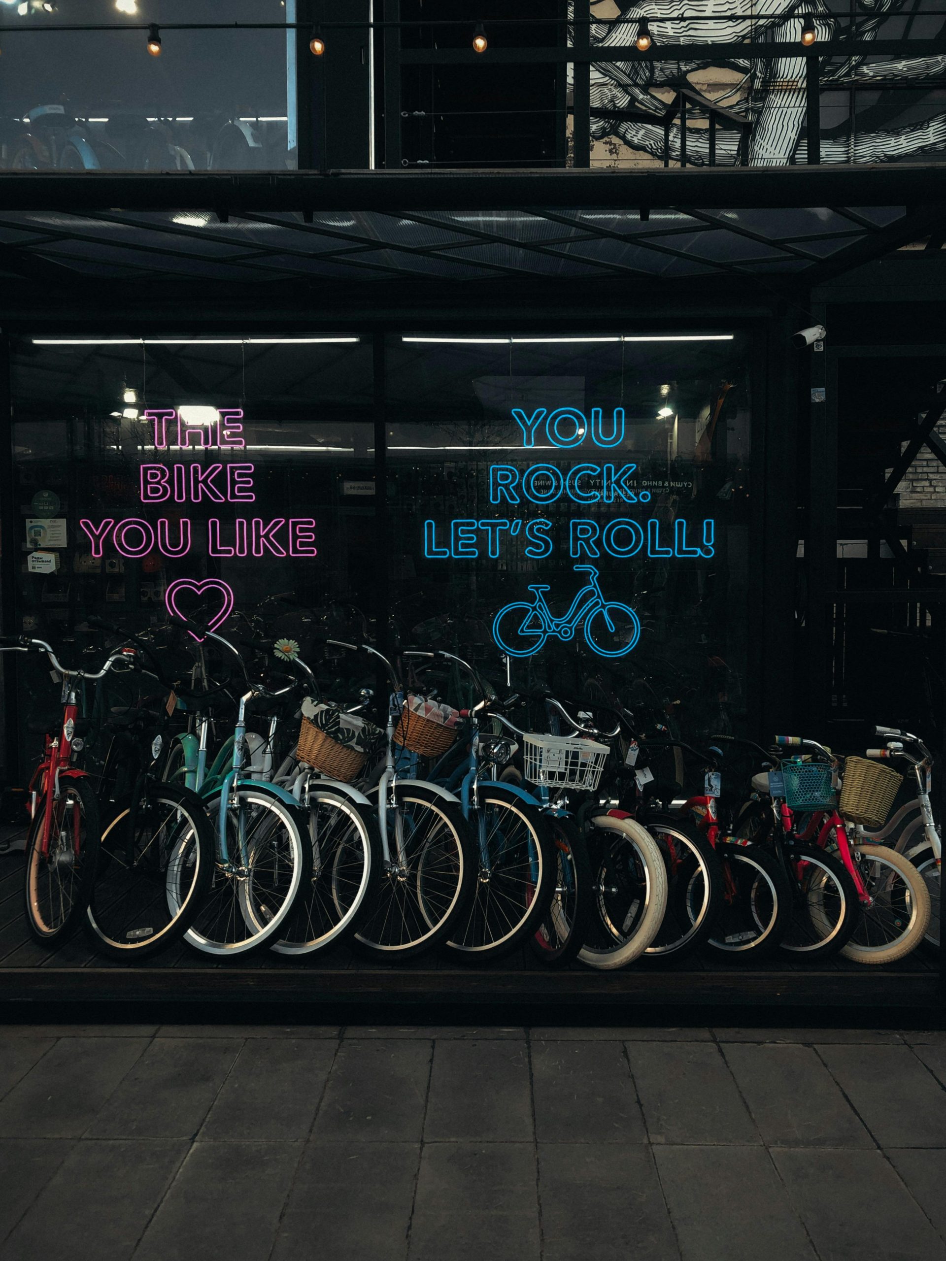 A vibrant row of bicycles for sale in an urban bike shop with neon signs at dusk.
