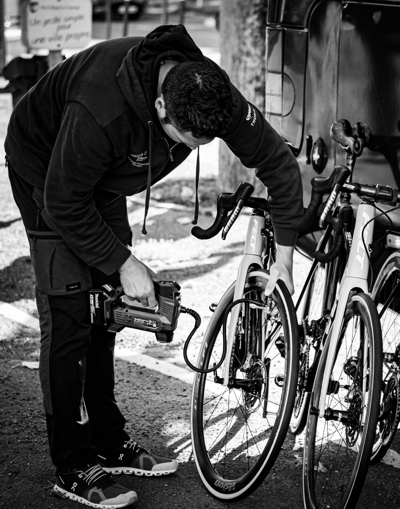 A man in a hoodie examining a row of road bicycles outdoors.