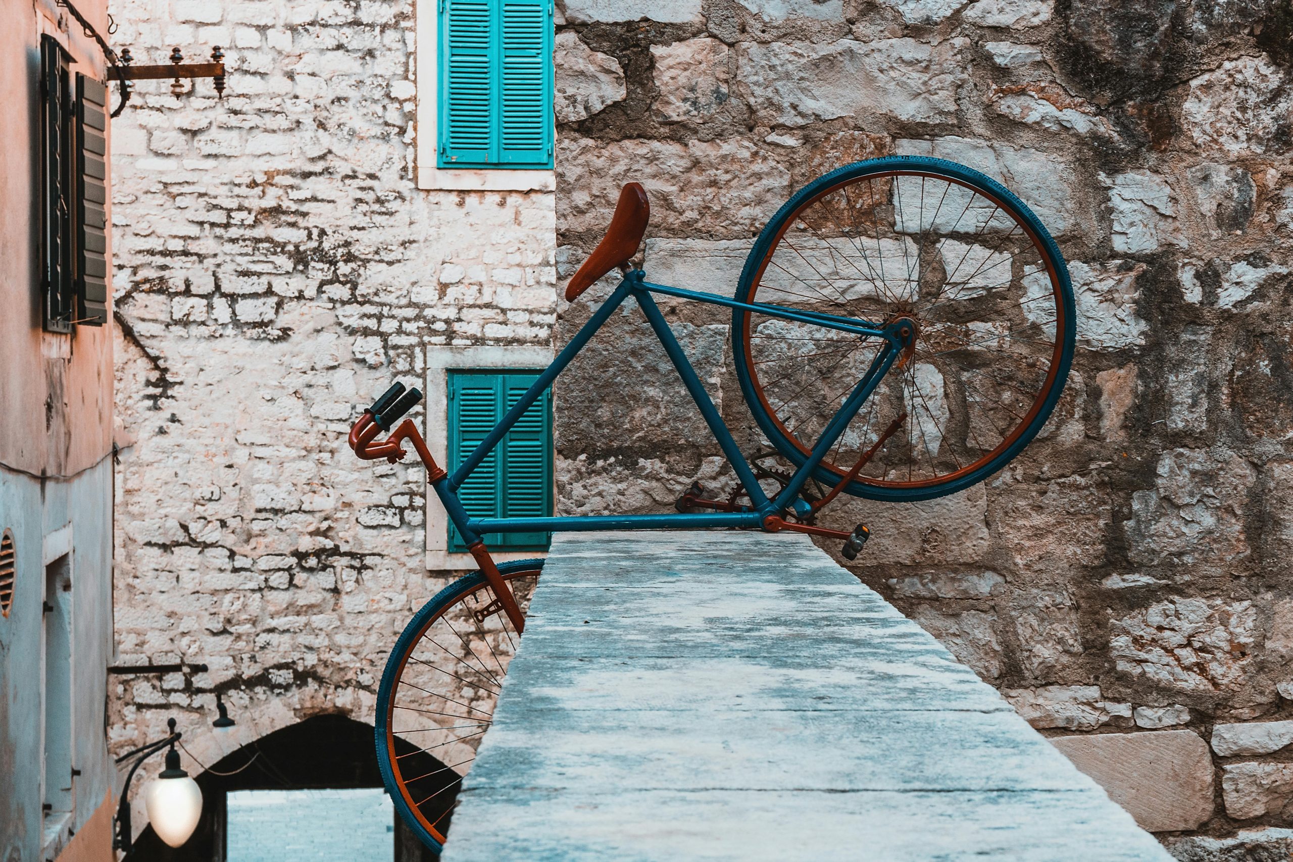 A retro bicycle leaning against a textured stone wall with vibrant shutters adds a classic urban charm.